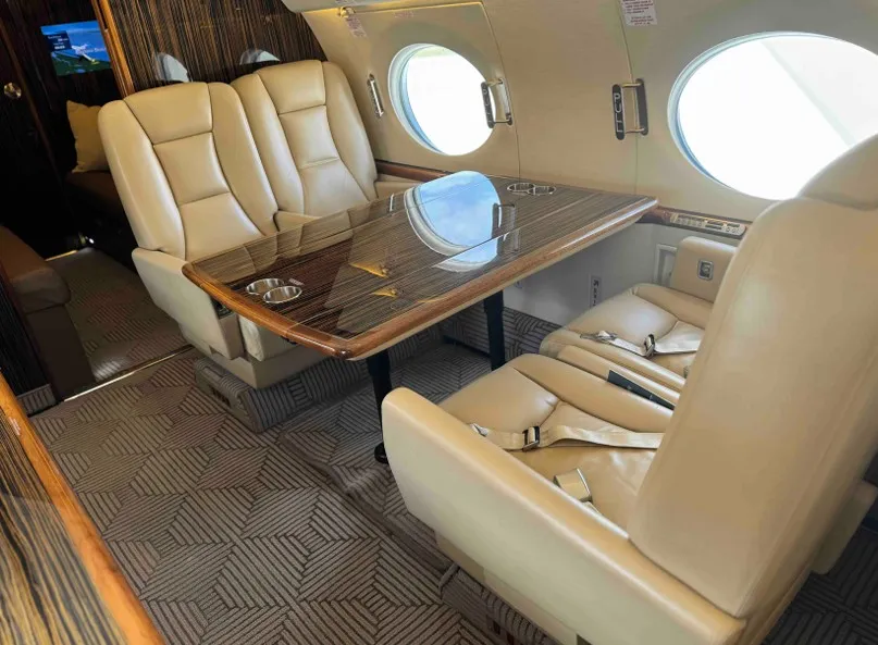 View from the front of the spacious Gulfstream G550 main cabin looking aft, featuring the forward four-seat club arrangement with plush beige leather seats.