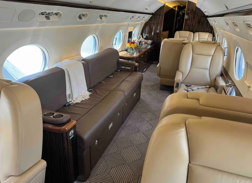 The four-place conference and dining area within the Gulfstream G550, showing the beige leather seats and a polished wood table set for work or a meal.