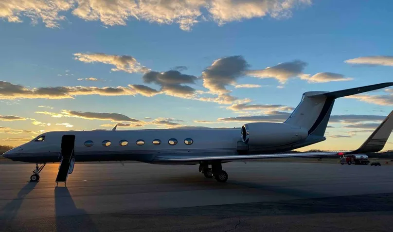 Exterior view of the 2009 Gulfstream G550 on the tarmac at sunset, with its boarding stairs deployed and ready for passengers.