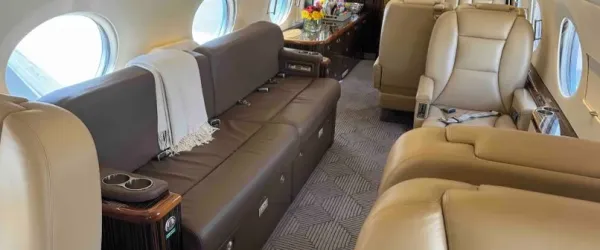 The four-place conference and dining area within the Gulfstream G550, showing the beige leather seats and a polished wood table set for work or a meal.