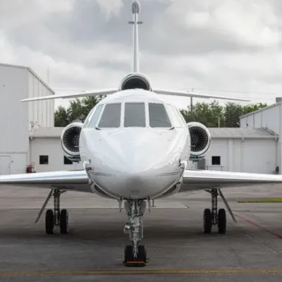 Head-on exterior view of the 2002 Falcon 50EX private jet parked on the tarmac in front of an aircraft hangar.